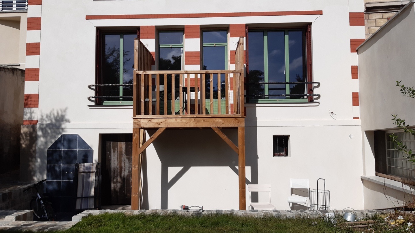 Balcon en bois sur poteaux avec garde-corps à barreaux, posé sur une façade de maison