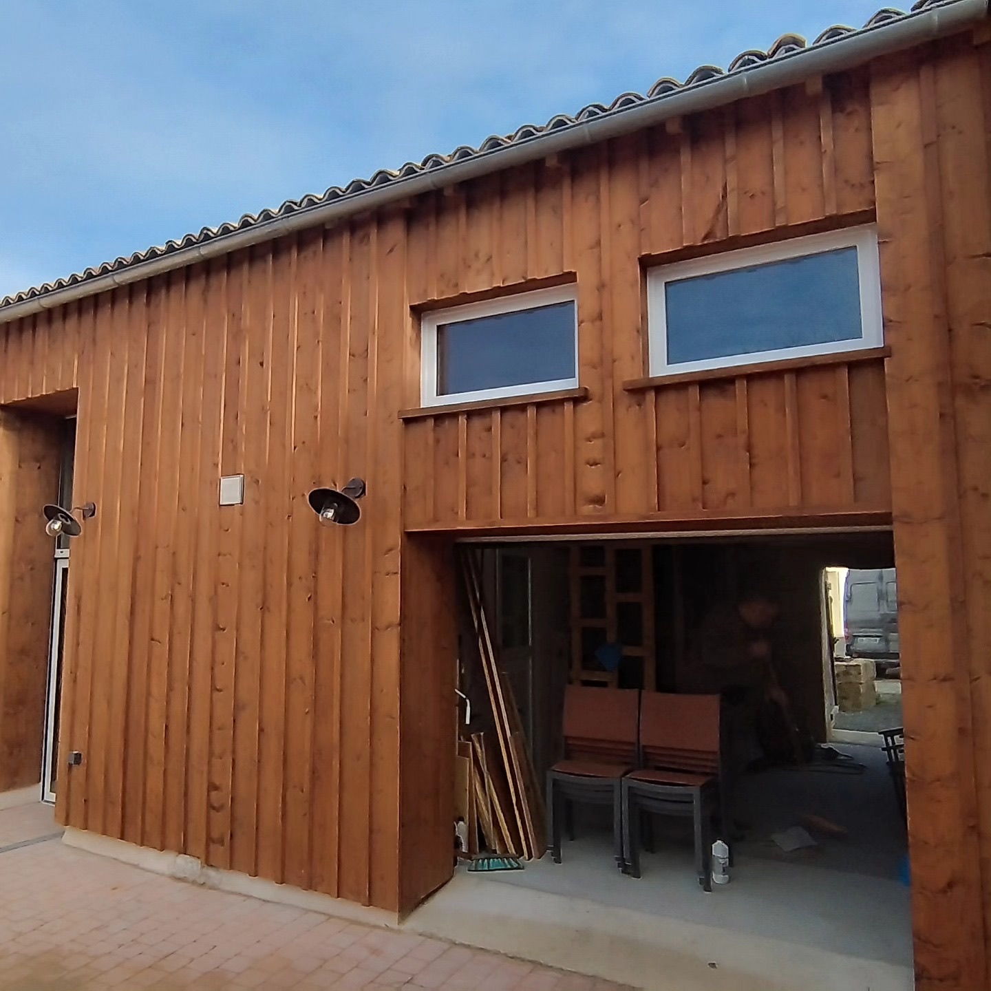 Façade d'atelier entièrement habillée d'un bardage bois vertical avec fenêtres et grande porte