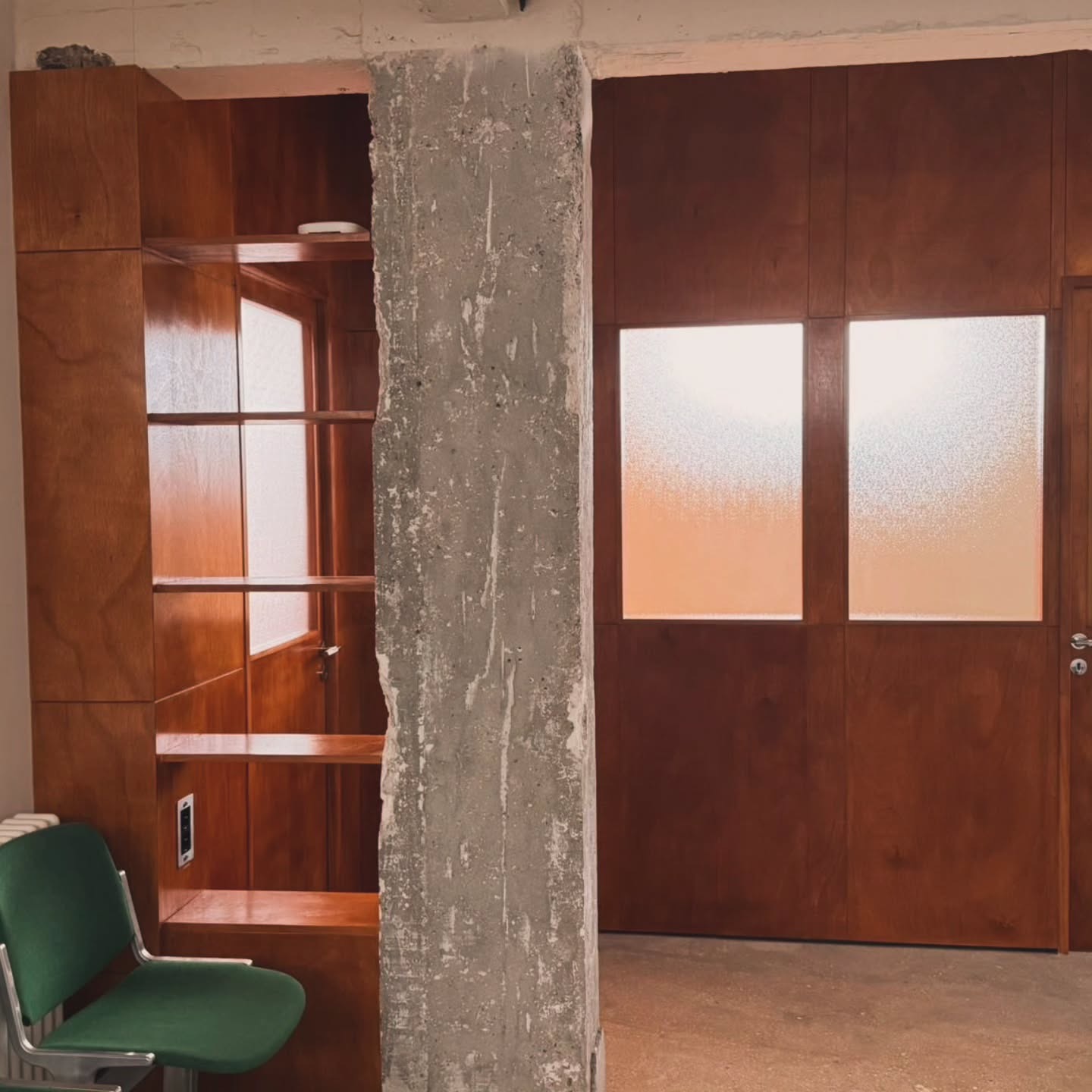 Boiserie murale en bois verni avec niches autour d'un poteau béton et double porte vitrée