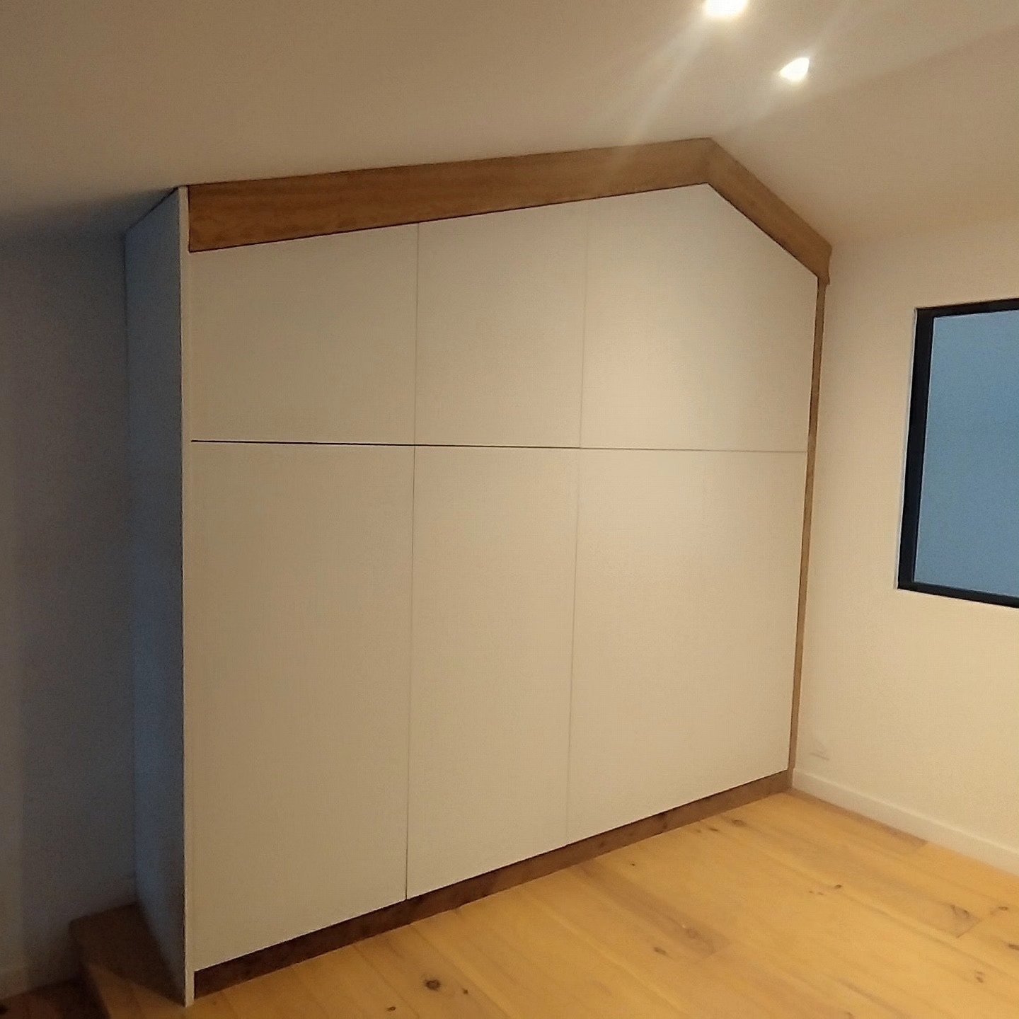 Placard sur mesure sous pente de toit avec façades blanches et bandeau en bois