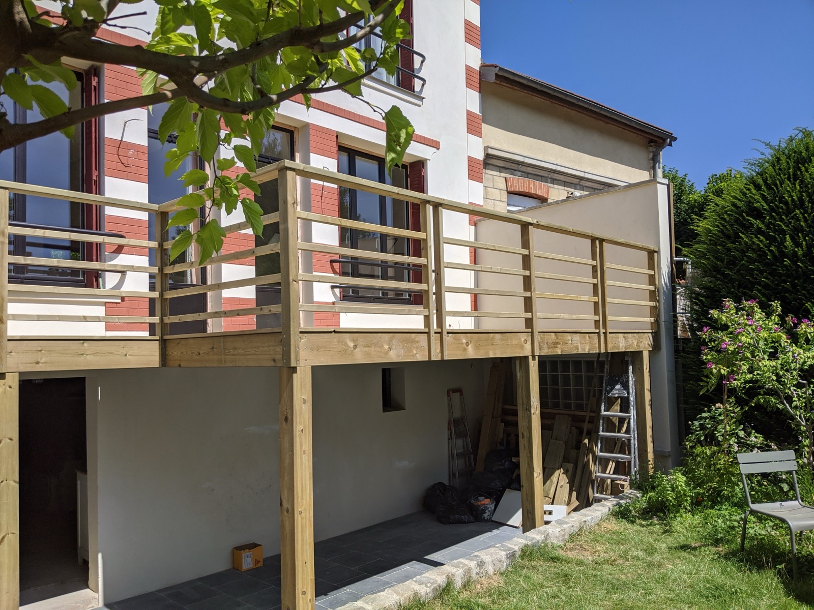 Terrasse suspendue en bois sur poteaux avec garde-corps, vue depuis le jardin
